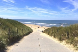 A concrete pathway leading to a beach with grassy banks on either side. - Holiday home in Den Helder with barbecue (Den Helder)