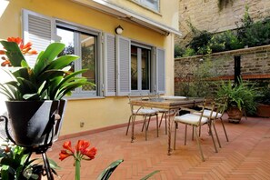 Eine Terrasse mit Tisch und Stühlen, einem Blumentopf und einem Fenster mit Rollläden.