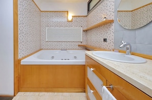 Ein modernes Badezimmer mit freistehender Badewanne, einem Waschbecken, Holzschränken, einem Spiegel und einer Wandleuchte.