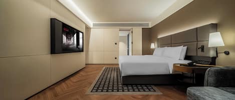 A hotel room with a bed, bedside table, lamp, and a television mounted on the wall.