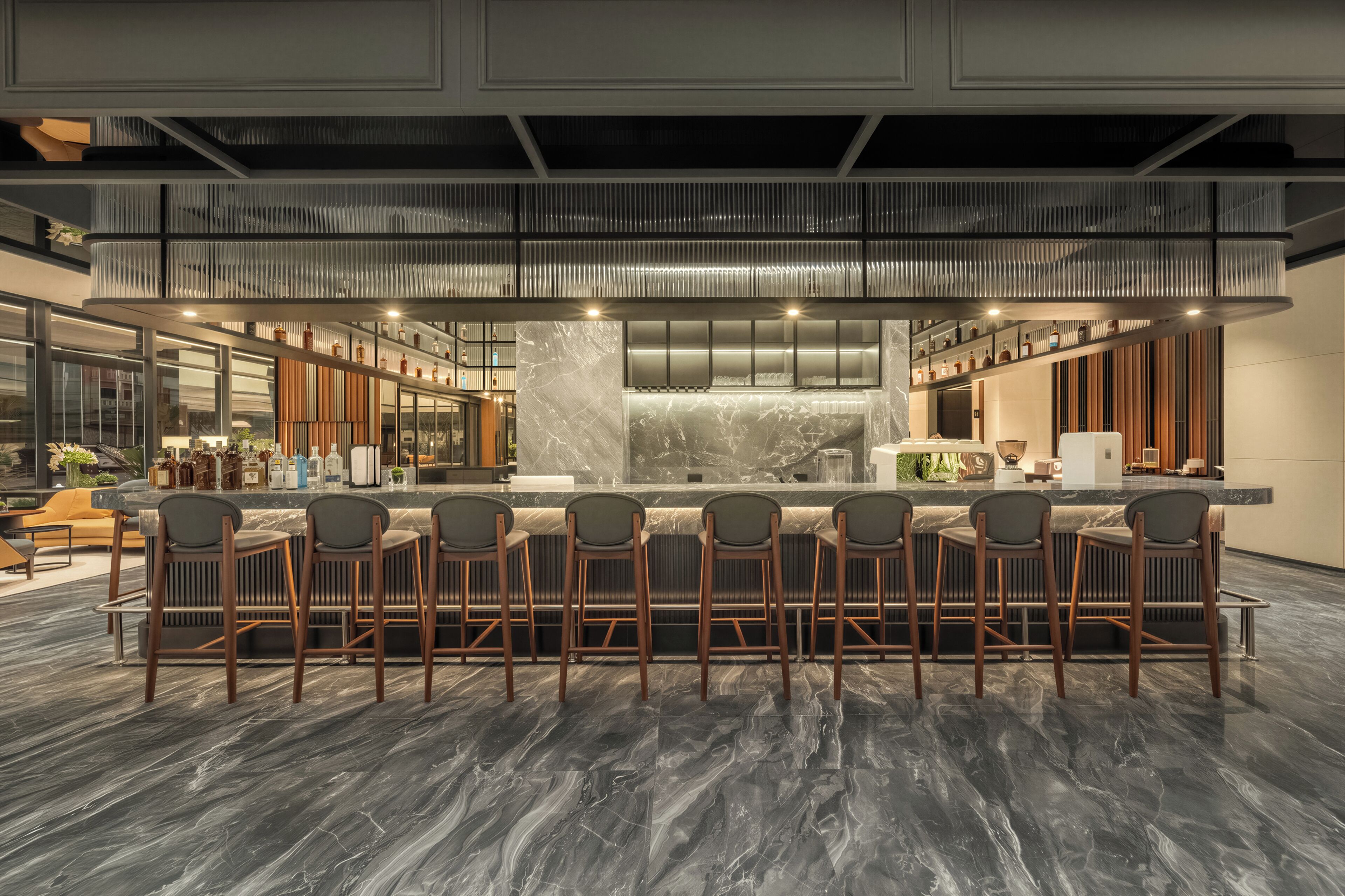 Zona bar moderna con un bancone in marmo, diversi sgabelli da bar e un soffitto alto dal design originale.