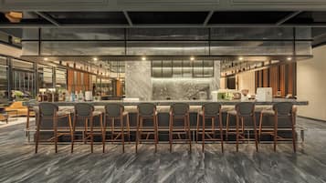 Zona bar moderna con un bancone in marmo, diversi sgabelli da bar e un soffitto alto dal design originale.