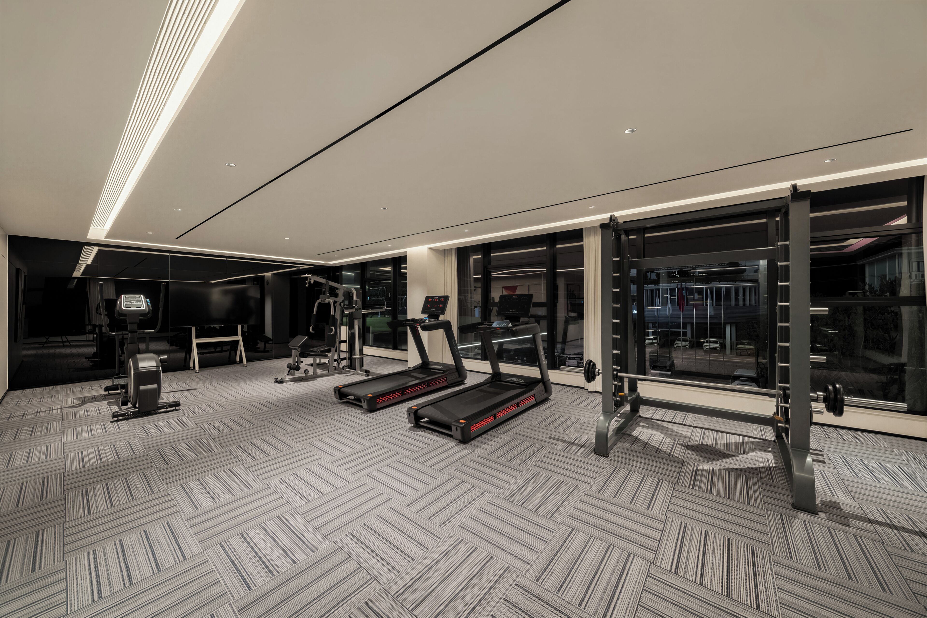 Un gimnasio moderno con cintas de correr, máquinas de pesas y un espejo grande.