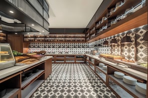 Una cocina moderna con piso de diseño geométrico, muebles de madera y diversos alimentos exhibidos en estantes y mostradores.