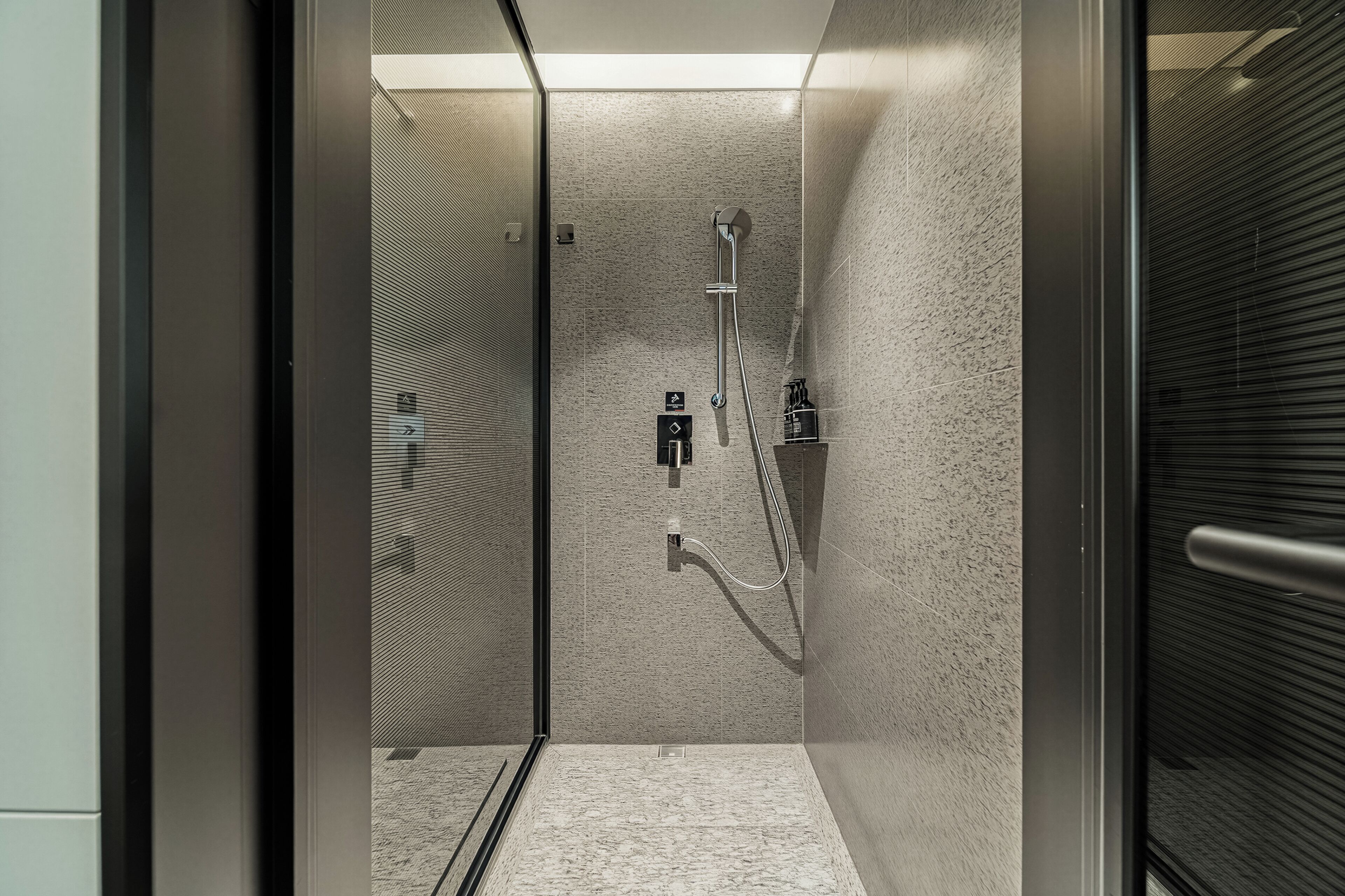 A modern shower area with a textured wall, a handheld showerhead, and a wall-mounted faucet.