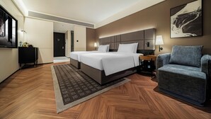 A hotel room with a large bed, a seating area, a desk, and a television.
