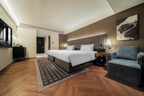 A hotel room with a large bed, a seating area, a desk, and a television.