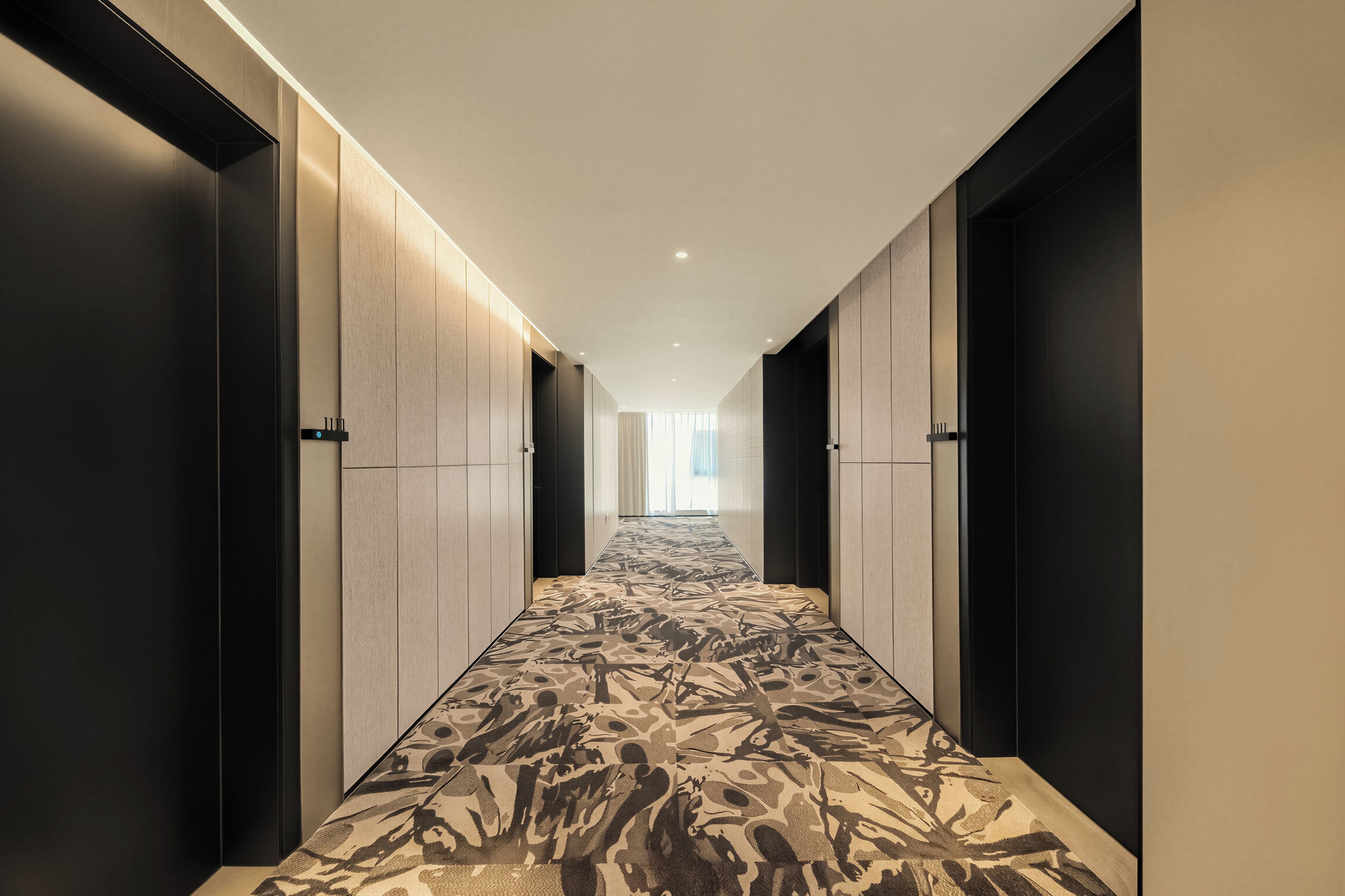 A hallway with a patterned carpet, doors on both sides, and a view into a room at the end.
