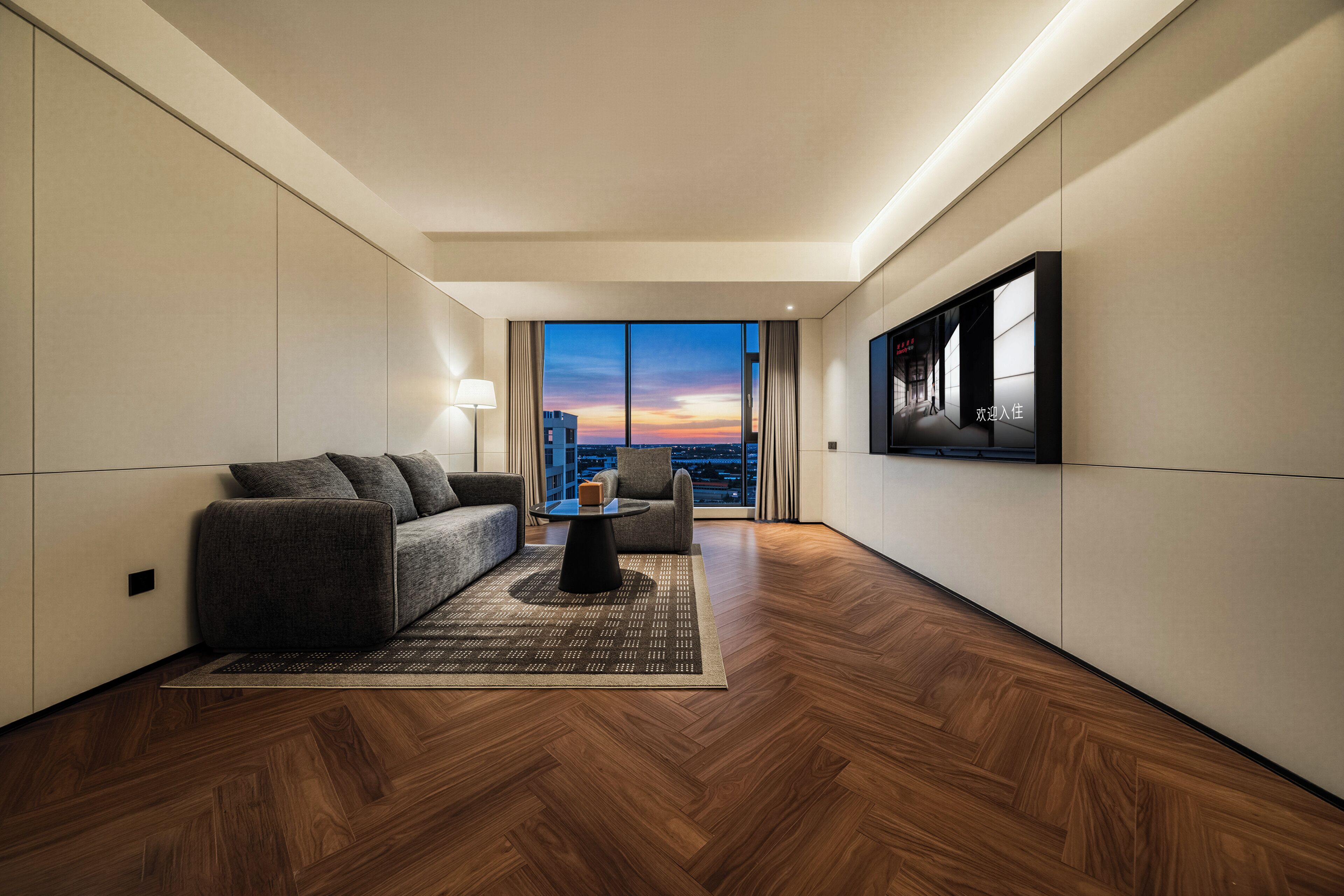 A modern hotel room with a sofa, a coffee table, and a large window offering a city view.