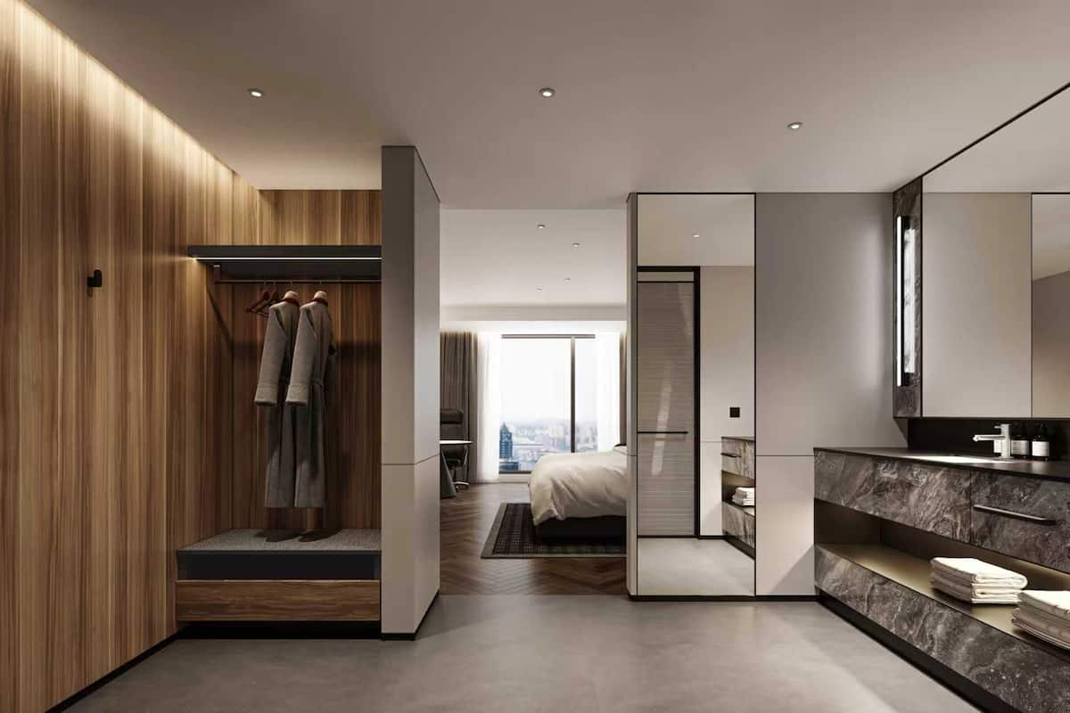 Ein modernes Hotelzimmer mit einem Holzschrank, einem Bett mit Blick auf die Stadt, einem Badezimmer mit Marmorwaschtisch und einem großen Spiegel.