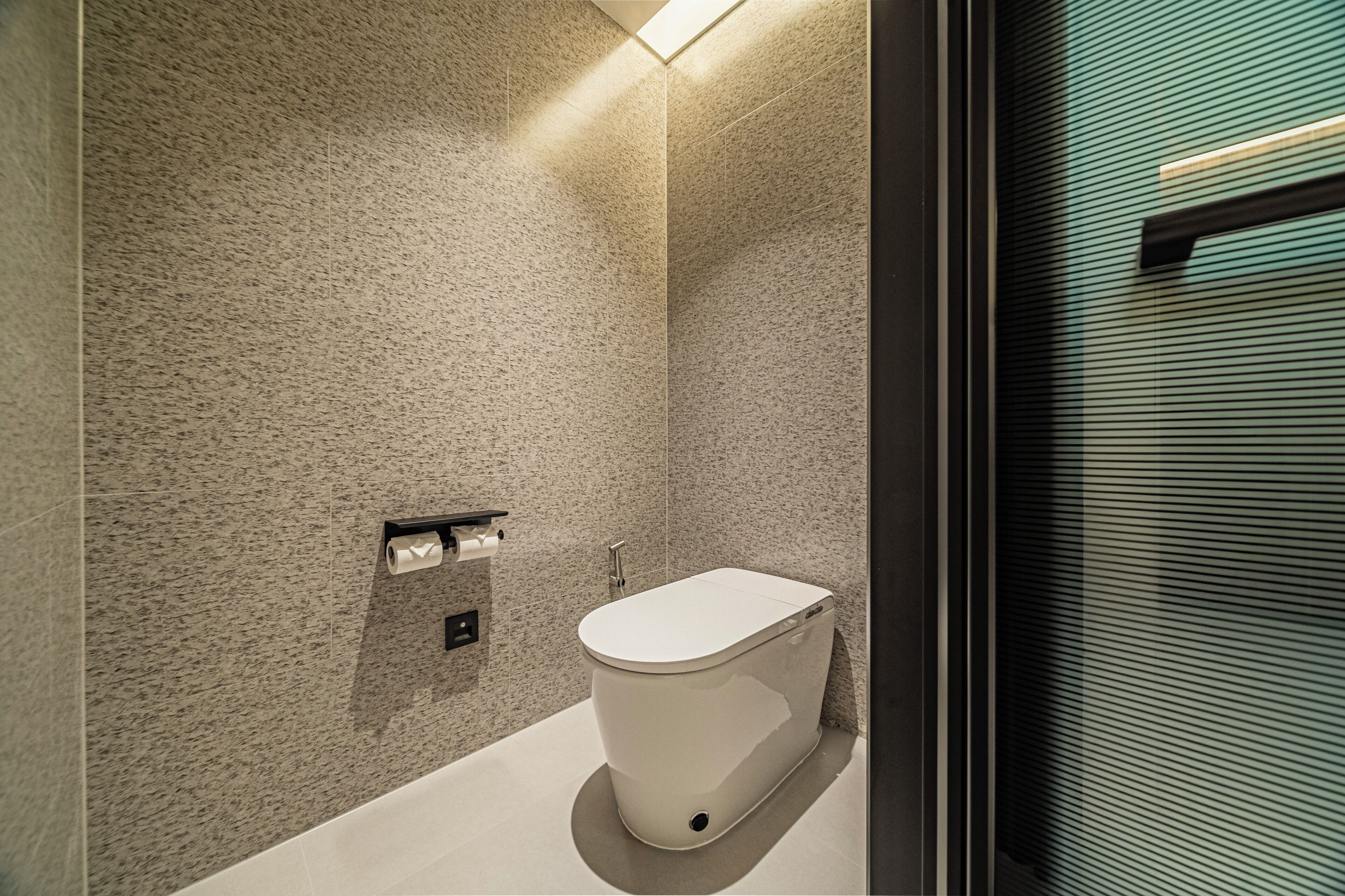 Een moderne badkamer met een wit toilet, een handdoekdispenser en een douchehoek.