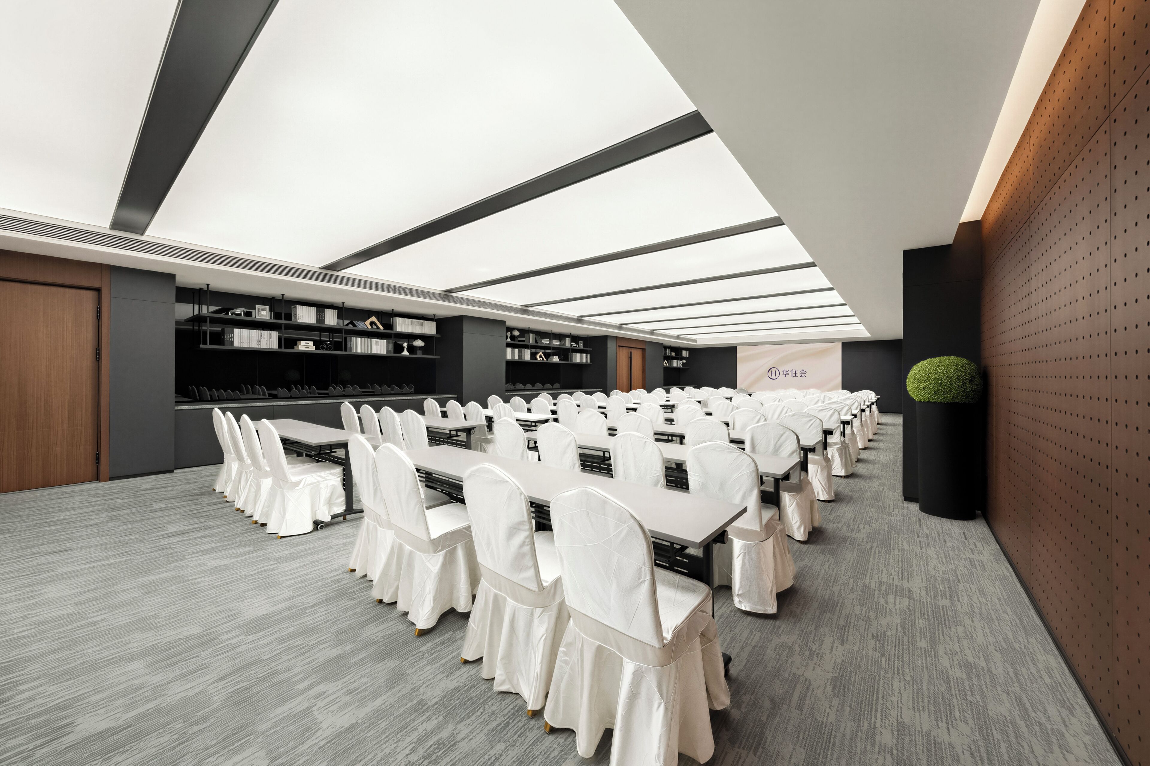 Une salle de conférence dotée de plusieurs tables et chaises, d’un plafond agrémenté de lucarnes et d’un mur sur lequel est affiché un panneau.