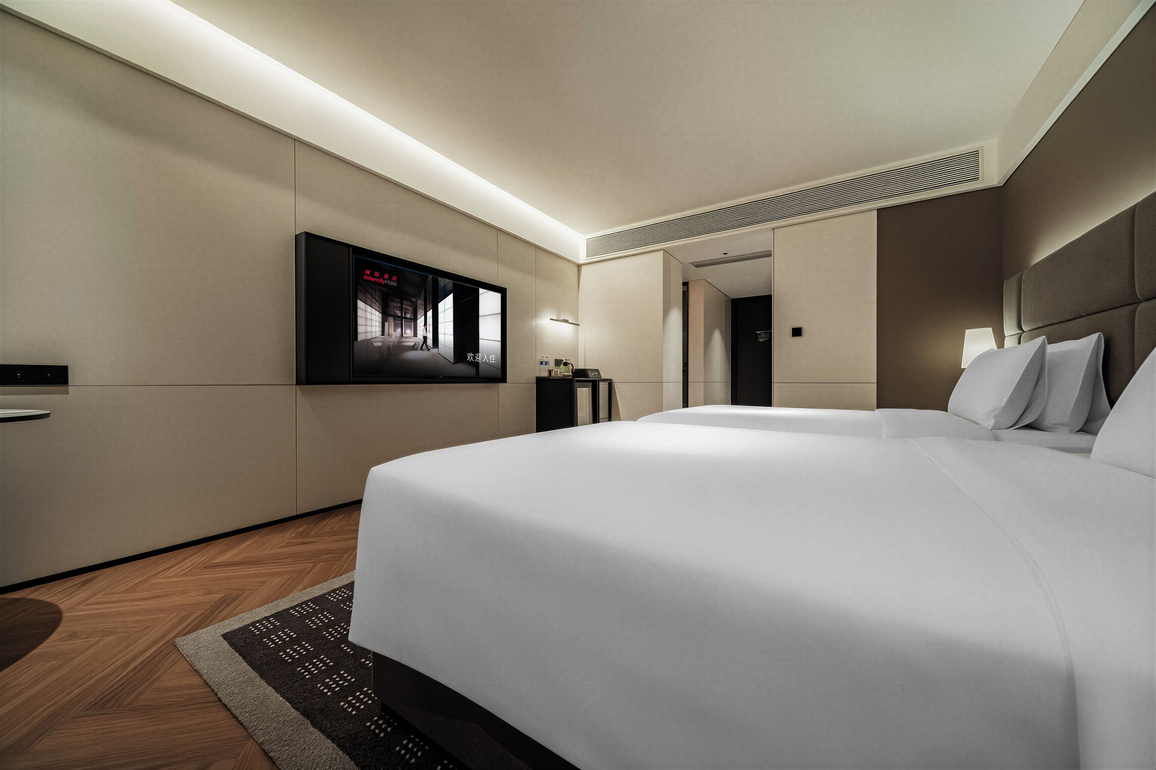 A modern hotel room with a large bed, a flat-screen TV mounted on the wall, and a wooden floor.