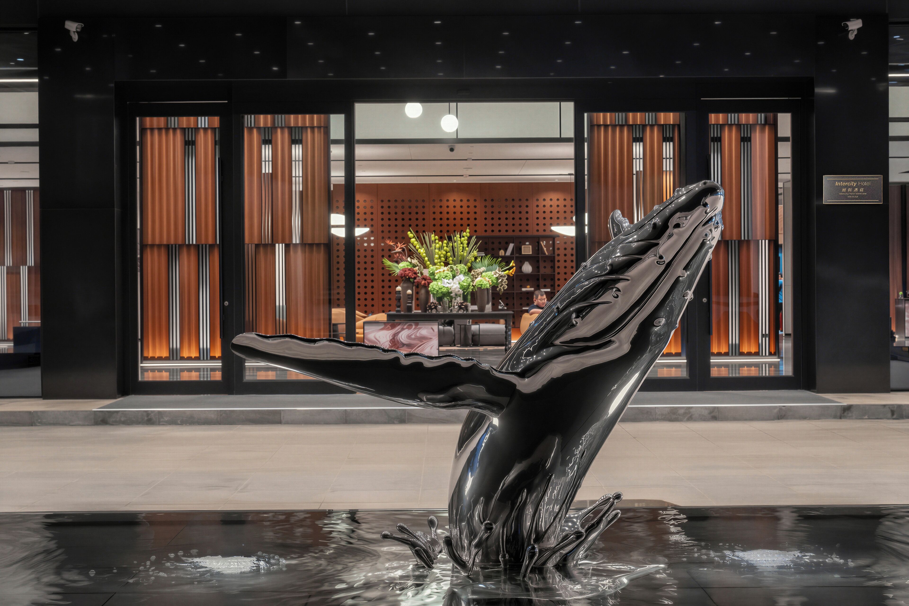 Un hall d’hôtel moderne avec une sculpture de baleine dans un élément décoratif aquatique, des panneaux de bois et un comptoir d’accueil.