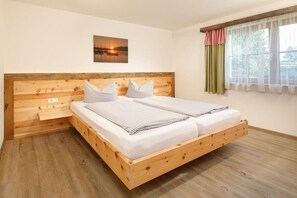 Ein hölzernes Bett mit zwei Kissen und einer Decke, ein Holz-Kopfteil, ein Bild an der Wand und ein Fenster mit Vorhängen.