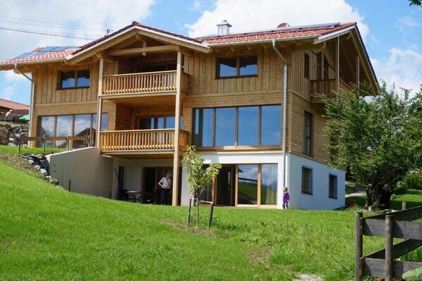 Ein zweigeschossiges Holzhaus mit Balkonen, großen Fenstern und einem Rasen.