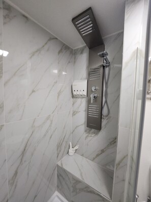 Ein Badezimmer mit Dusche, Marmorfliesen, Bedienfeld und einem Handtrockner.