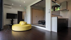 A modern living room with a yellow sofa, a flat-screen TV, and a dining area with a table and chairs.