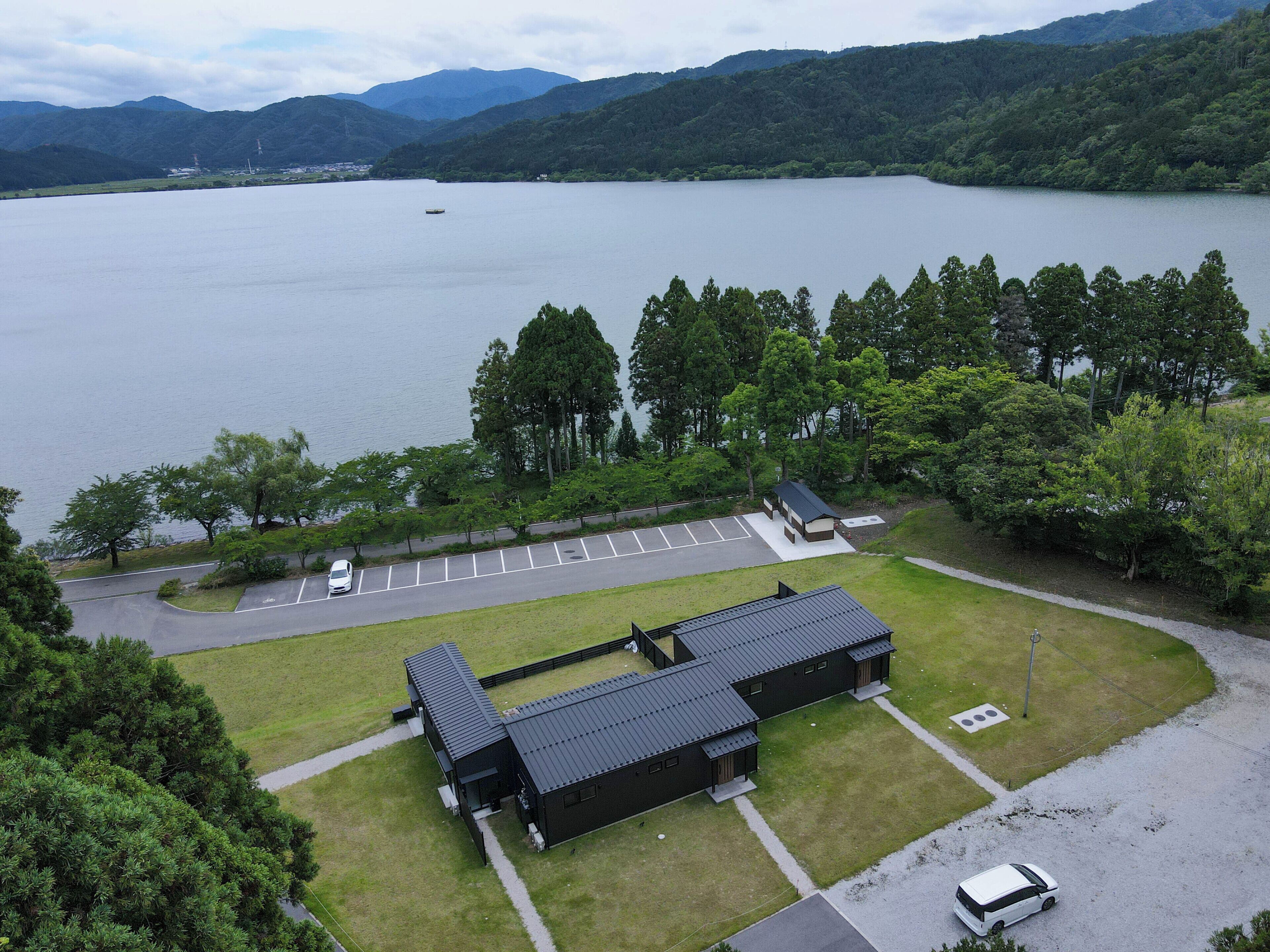 Un bâtiment doté d’un toit plat, situé à côté d’un parking avec des places délimitées, et avec une étendue d’eau en arrière-plan.