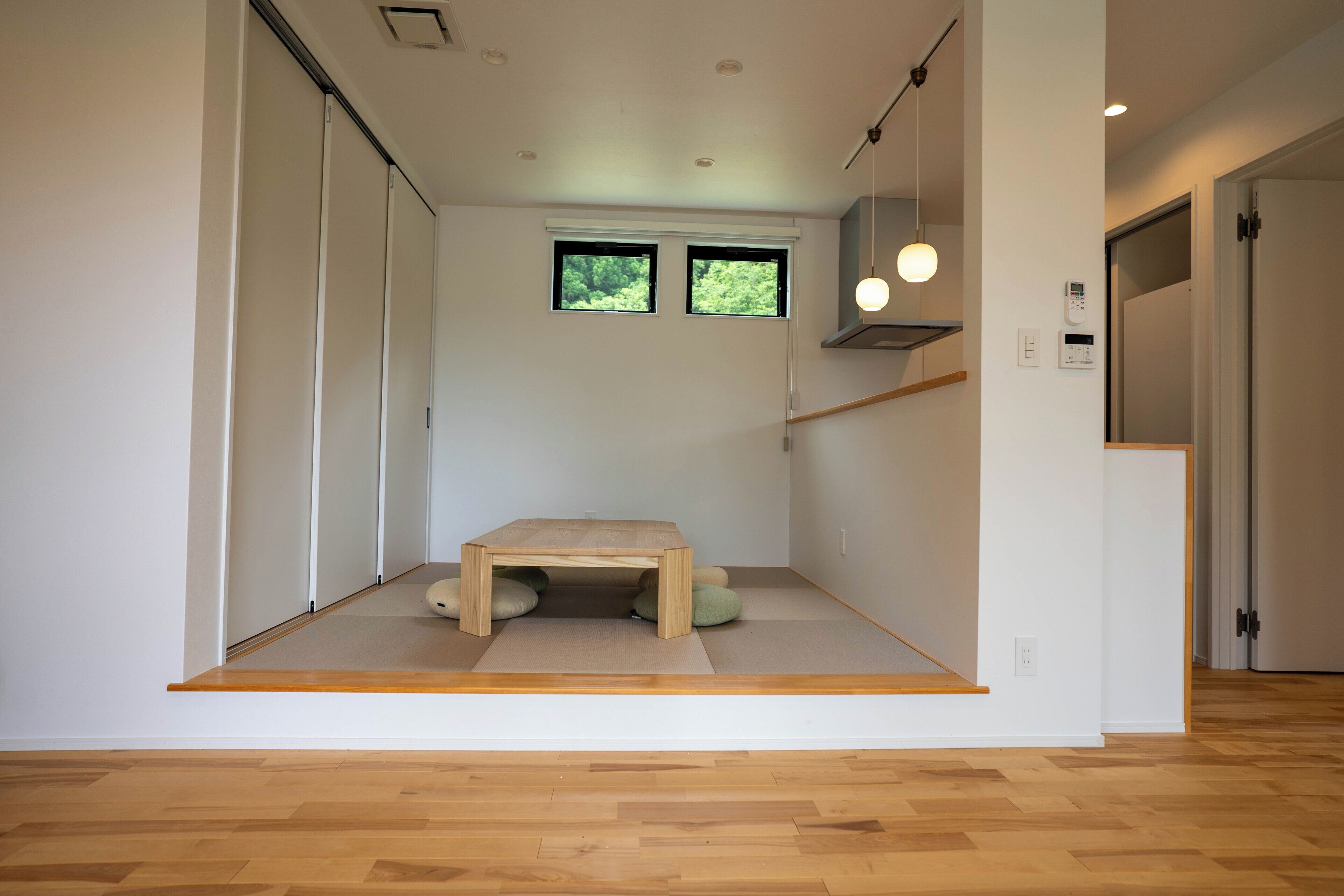 Een minimalistisch ingerichte kamer met een lage houten tafel, tatami matten, een klein raam en een plafondlamp.