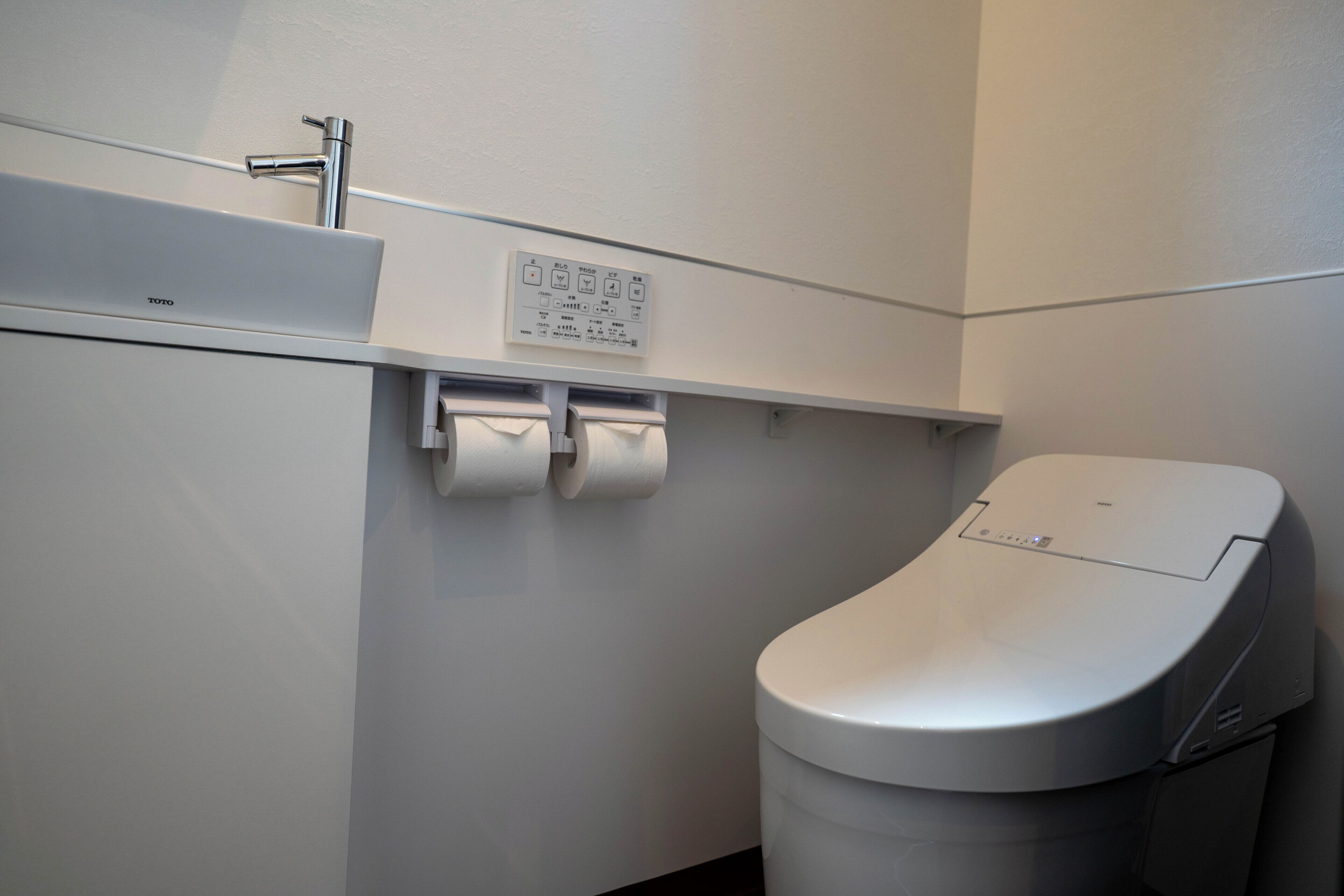Un inodoro moderno con panel de control, un lavamanos y un dispensador de toallas de papel en un baño.