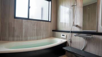 A modern bathroom with a freestanding bathtub, a shower, and a window.