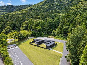 A modern building with a flat roof, surrounded by a parking lot and lush greenery. - Yogo Lakeside Villa Kagamigaoka (Nagahama)