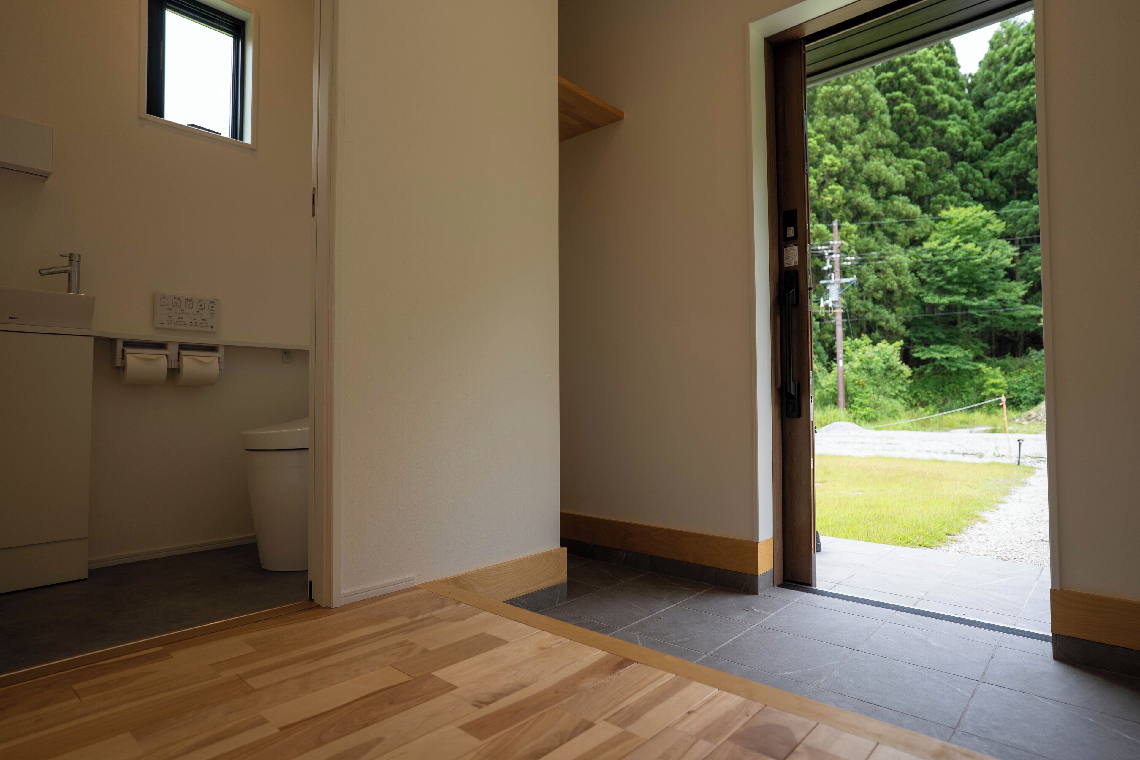 A hotel room with a wooden floor, a toilet, a sink, and a window with a view of trees.