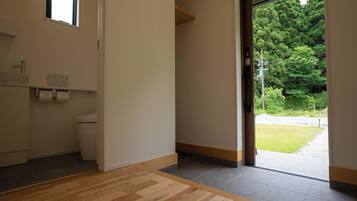 A hotel room with a wooden floor, a toilet, a sink, and a window with a view of trees.