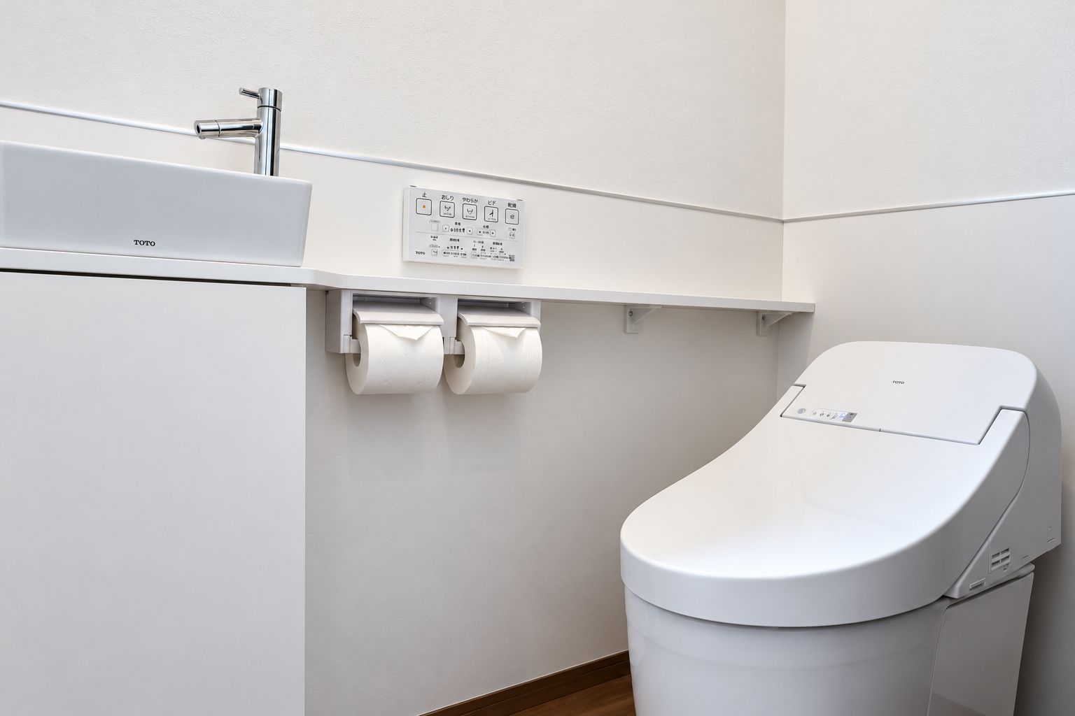 Moderni wc, jossa on ohjauspaneeli, seinään kiinnitetty wc-paperiteline ja pesuallas hanalla.