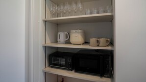 A kitchen with a coffee maker, a microwave, and a shelf with wine glasses.