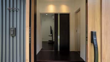 Un pasillo con una puerta de madera a la derecha, suelo oscuro y un interruptor de luz en la pared.