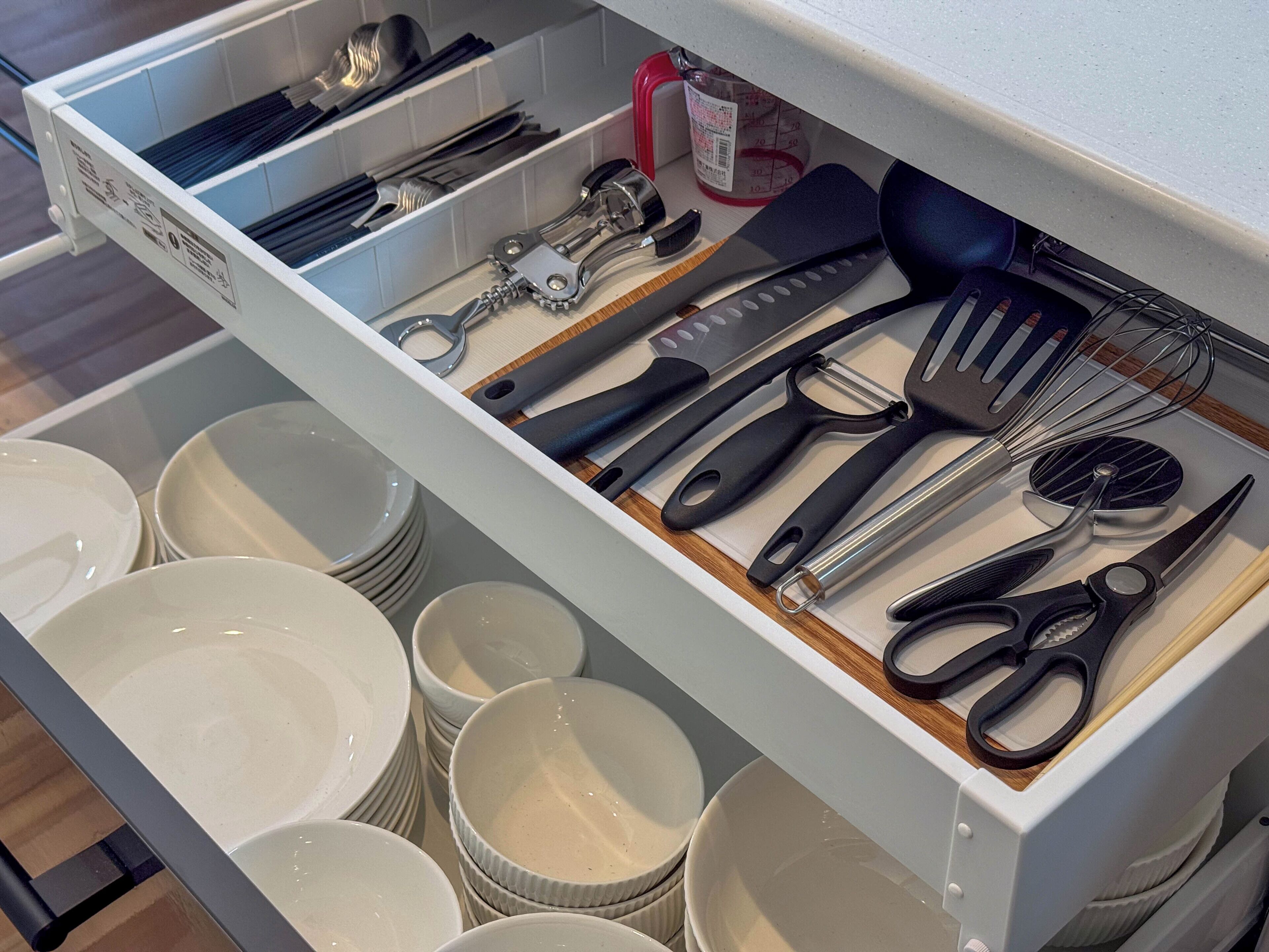 A drawer with kitchen utensils, including a whisk, spatula, and scissors.