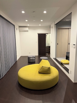 A modern interior with a circular yellow seating area, a dark wooden floor, and a sliding door. - Yogo Lakeside Villa Kagamigaoka (Nagahama)