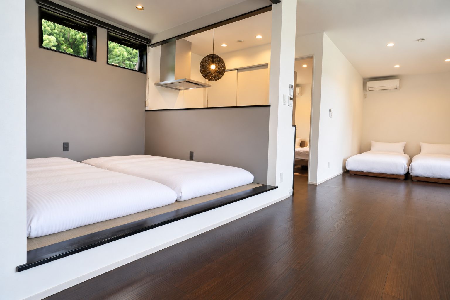 Habitació d'hotel moderna amb un llit gran, una cadira arrossada, una làmpada penjant i vista cap a l'exterior.