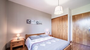 Quarto com cama de madeira, duas mesas de cabeceira, luminária pendente e um guarda-roupa.