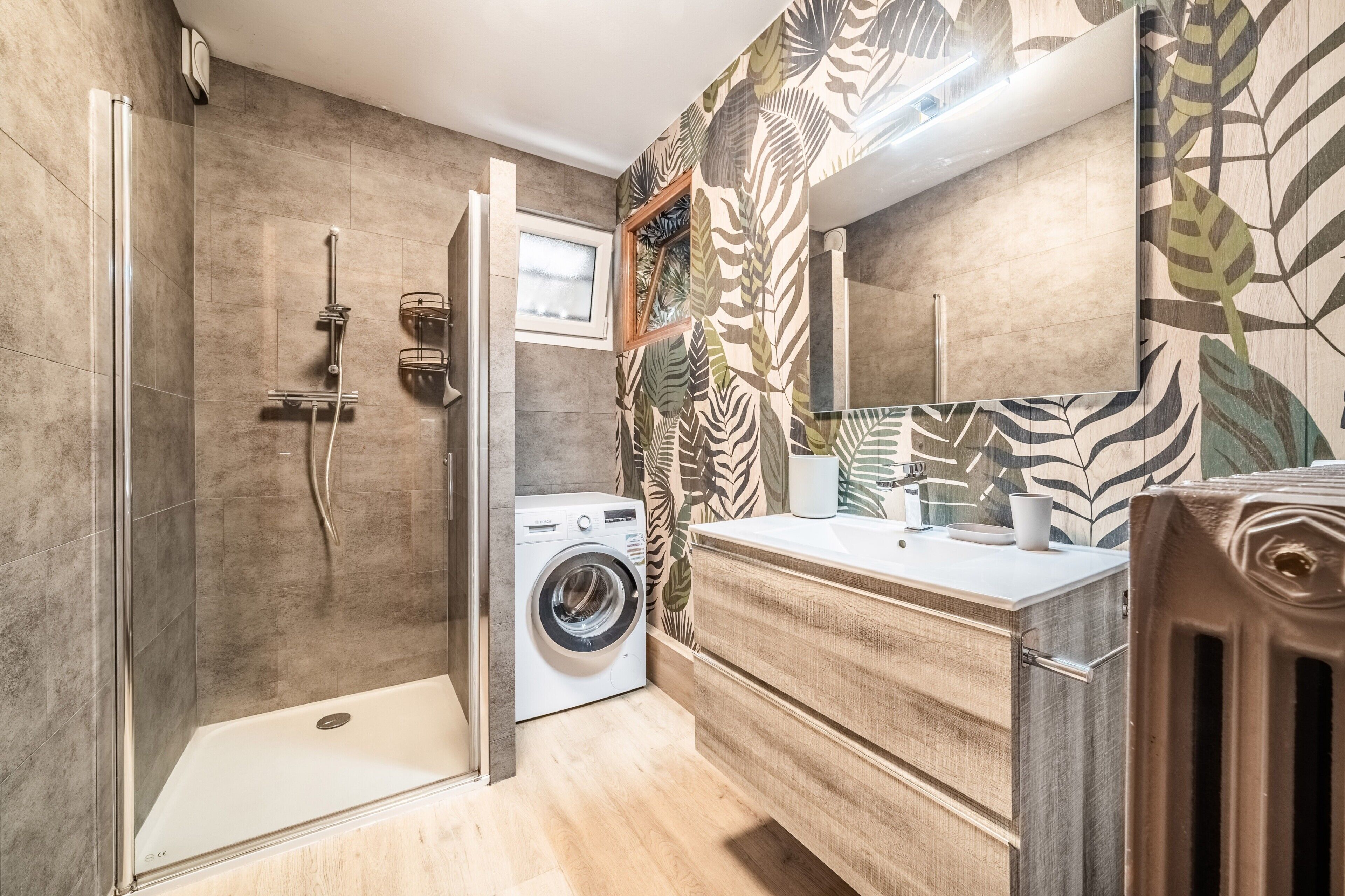 A modern bathroom with a glass shower enclosure, a Bosch washing machine, and a wooden vanity.