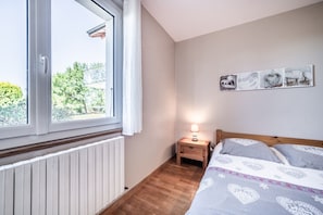 A bedroom with a large window, a bedside table with a lamp, and a bed with patterned bedding.