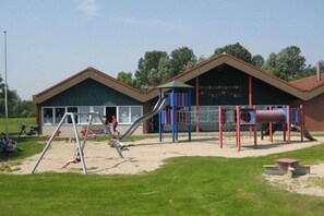Ein Spielplatz mit Schaukeln und Rutschen, ein Gebäude mit einem Schild und eine Rasenfläche.