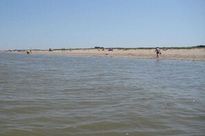 Ein Strand mit ruhigem Wasser, sandigem Ufer und Zelten in der Ferne.