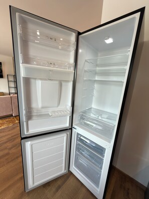 Ein offener Kühlschrank mit mehreren Regalen und Schubladen, einem Wasserspender und einem Gefrierfach.