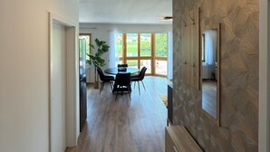 Um interior moderno com piso de madeira, uma área de jantar com mesa e cadeiras, e uma janela grande que permite entrada de luz natural.