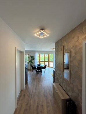Ein modernes Interieur mit Holzboden, einer Essecke mit Tisch und Stühlen sowie einem großen Fenster, das für natürliches Licht sorgt.