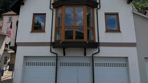 Um edifício de dois andares com varanda saliente, garagem com portão basculante e céu claro.