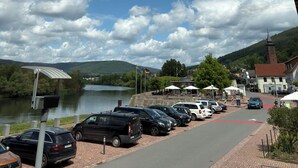 Uma área de estacionamento com carros, um corpo d'água e um edifício com telhado vermelho ao fundo.