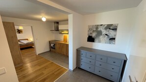 Une cuisine moderne avec un four encastré, un plancher en bois, un meuble gris et un tableau accroché au mur.