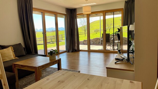 Un salon moderne avec un canapé, une table basse et une vue sur un paysage verdoyant, visible à travers de grandes portes-fenêtres coulissantes.