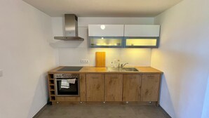 Une cuisine compacte dotée d’un four encastré, d’une plaque de cuisson, d’un évier et d’armoires en bois.