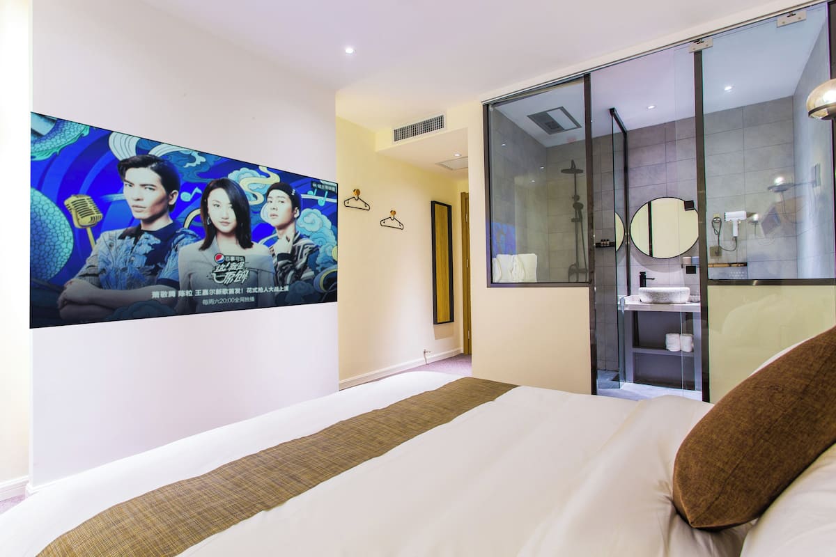 Habitación de hotel con una cama grande, cabina de ducha de vidrio, televisor montado en la pared y baño con espejo y lavamanos.