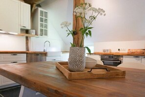 A wooden kitchen counter with a ceramic vase holding white flowers, a wooden tray, and a white bowl.